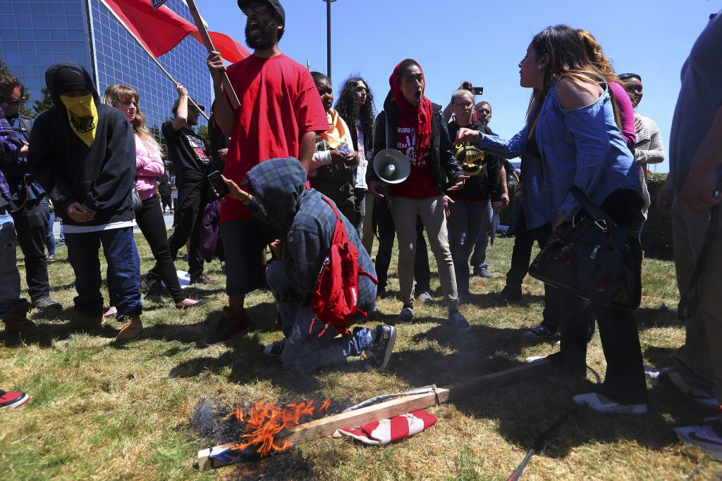 Over the strong objections of the woman at right, protesters burn an American flag outside the Hyatt Regency in Burlingame, Calif., where Donald Trump addressed the state Republican Party convention, April 29, 2016. Protesters also formed a human chain to block the hotel, and at one point, a group appeared to rush the entrance, but were repelled by police. (Jim Wilson/The New York Times)