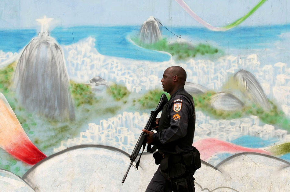 Duas cidades: policial fortemente armado passa em frente a painel na favela de Manguinhos, zona norte. Foto: WILTON JÚNIOR/AE