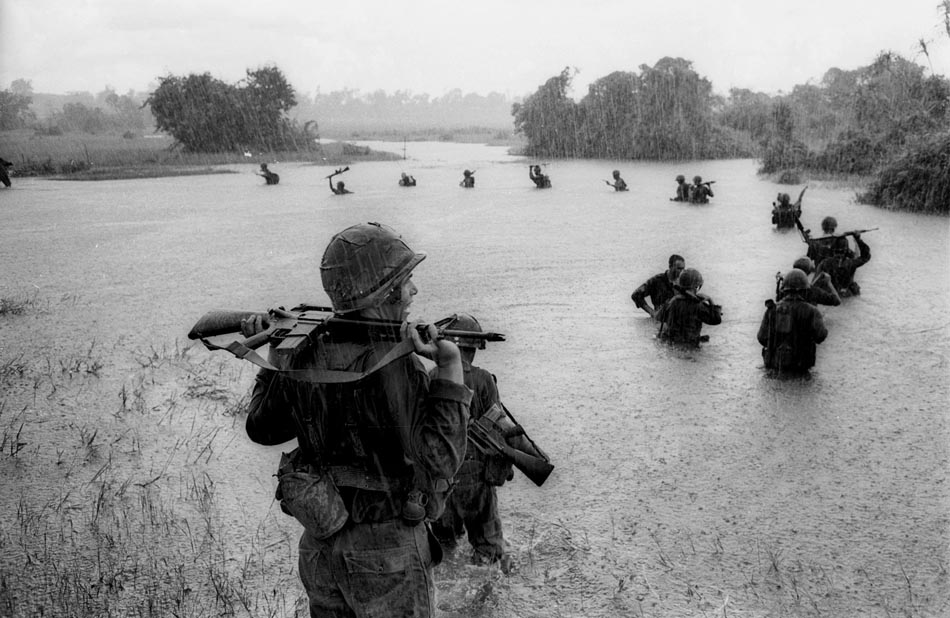 Homens do exército norte-americano atravessam rio em Ben Cat. 25/09/1965. Foto: Henri Huet/AP