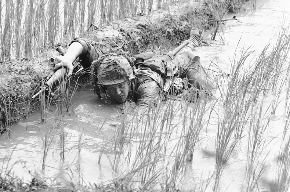 Militar norte-americano, Lacey Skinner, rasteja em plantação de arroz em Thi. 1966. Foto: Henri Huet/AP