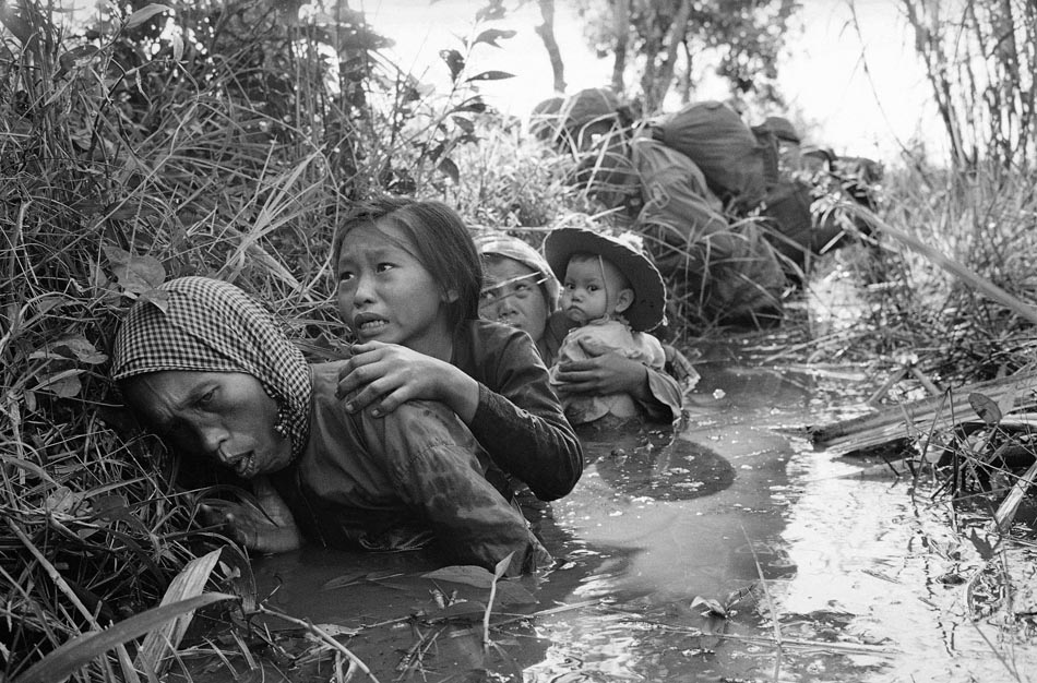 Mulheres e crianças buscam proteção em um canal lamacento, durante intenso fogo cruzado em Bao Trai cerca de 20 quilômetros a oeste de Saigon. 01/01/1965. Foto: Horst Faas/AP