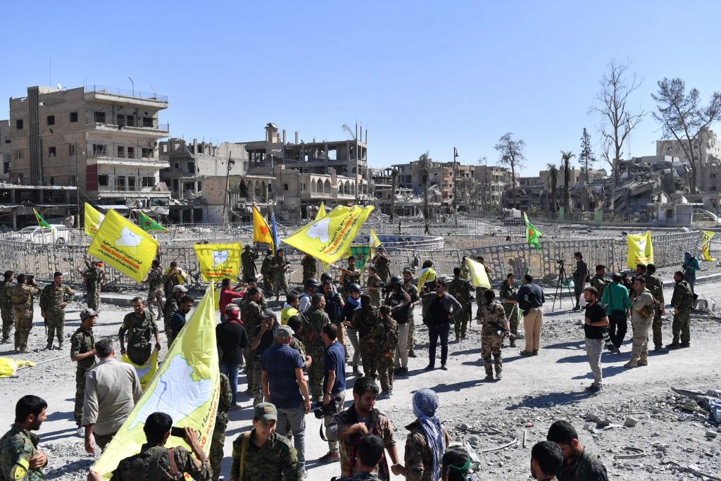 Combatentes curdos hasteiam bandeiras das Forças Democráticas Sírias (FDS) na Praça Naim, icônica localidade da cidade de Raqqa (AFP PHOTO / BULENT KILIC)