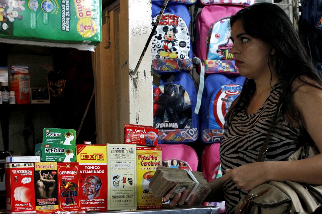 Venezuelana carrega pilha de notas de bolívares enquanto observa remédios em um mercado popular na cidade de Rubio (REUTERS/Carlos Eduardo Ramirez)